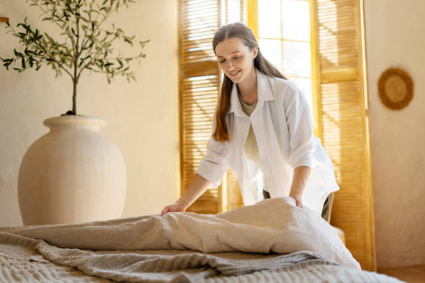 A woman is neatly placing a blanket on a bed as part of rental cleaning services.