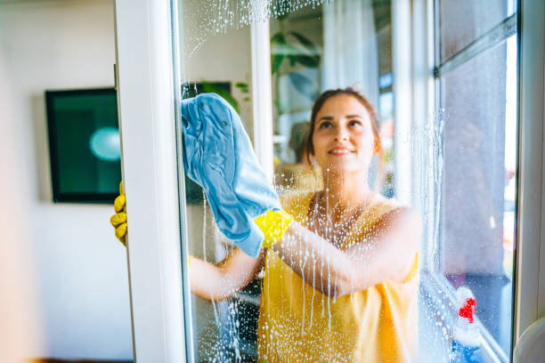 A woman diligently cleaning a window with a sponge, emphasizing a deep cleaning effort.