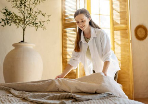 A woman is neatly placing a blanket on a bed as part of rental cleaning services.