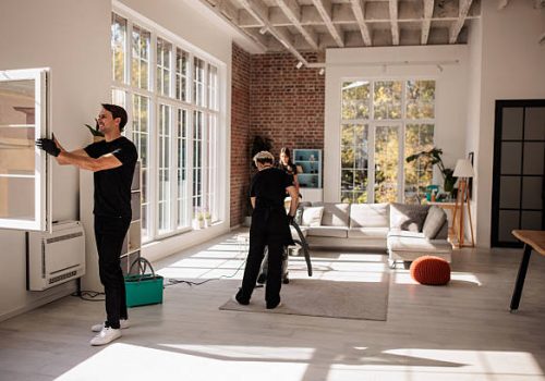 Two people from a professional maid service cleaning a room with a large window, ensuring a tidy and bright space.